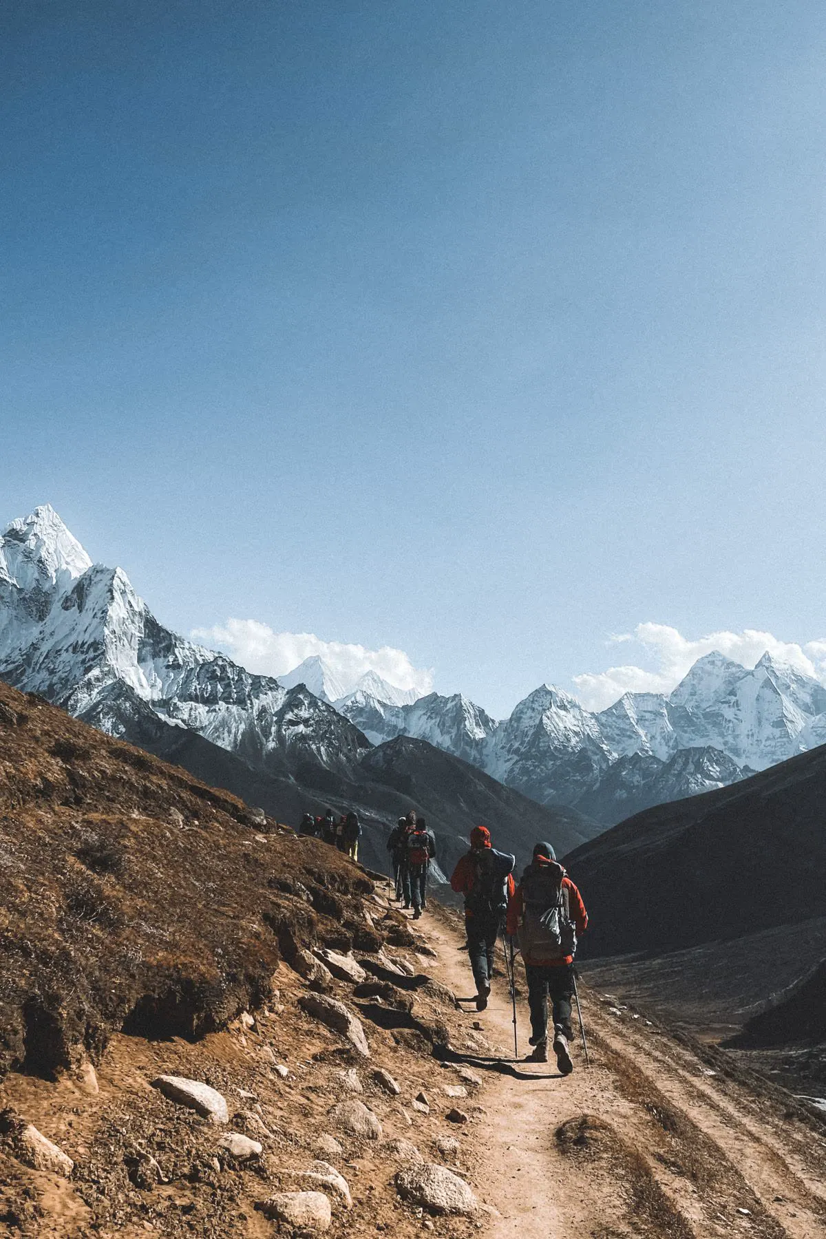 Trekkers walking a mountain trail beneath snow peaks